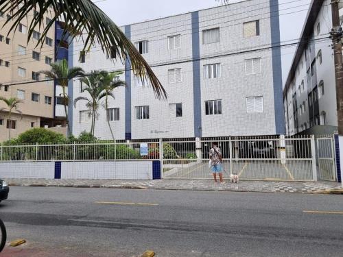 a person walking a dog on a sidewalk next to a building at Apartamento para alugar in Mongaguá