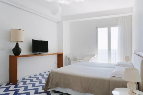 a white bedroom with a bed and a tv at Giuggiulena in Siracusa