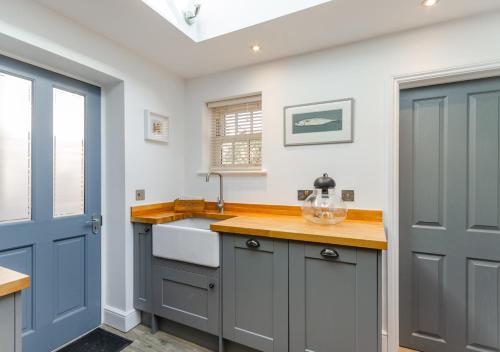 eine Küche mit einem Waschbecken und einer blauen Tür in der Unterkunft Postmans Cottage in Holt