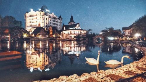 two white swans in a lake in front of a building at Etno selo Stanišići Hotel Ras in Dijelovi
