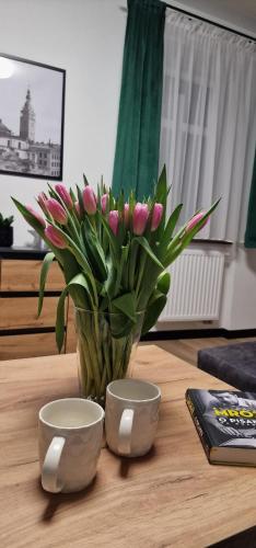 un jarrón de tulipanes rosas sobre una mesa con dos tazones en Apartament z duszą, en Kłodzko