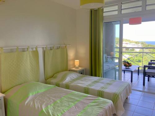 two beds in a bedroom with a view of a balcony at Orchidée, Spacieux & Vue mer in Les Trois-Îlets
