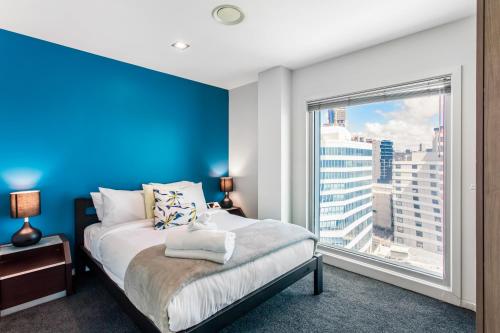 een slaapkamer met een blauwe accentmuur en een bed met een raam bij Urban Horizon with sea views and pool in Auckland