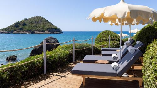 a row of lounge chairs with an umbrella and the ocean at La Roqqa in Porto Ercole