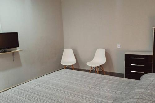a bedroom with a bed and two white chairs at Casa Magnolia in Tarija