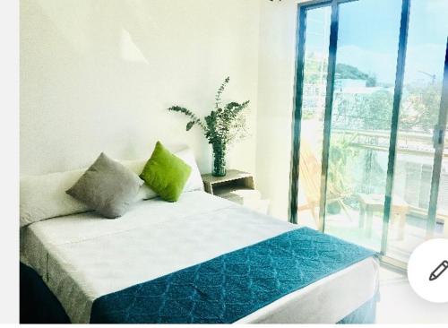sypialnia z łóżkiem z zielonymi poduszkami i oknem w obiekcie Casa Ohana By Utopia w mieście Playa del Carmen