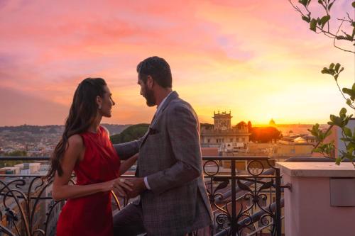un homme et une femme debout sur un balcon avec le coucher du soleil dans l'établissement Baglioni Hotel Regina - The Leading Hotels of the World, à Rome