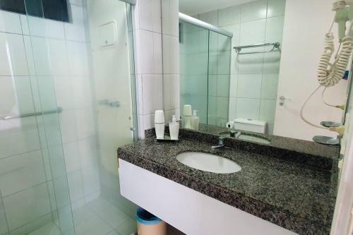 a bathroom with a sink and a shower with a mirror at Flat para 2, de frente para o Mar in Natal