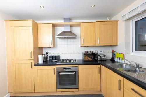 a kitchen with wooden cabinets and a sink at Spacious and Luxurious 5 Bedroom Town House for 9 in Kent