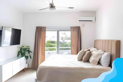 a white bedroom with a bed and a television at Minimalist Studio with Pool and FREE Scooter in Cozumel