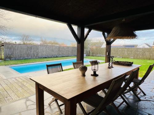 una mesa de madera y sillas en un patio con piscina en ZEN Op Vakantie @vakantiehoeve met zwembad en Lierde