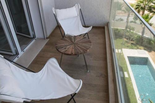 einen Balkon mit 2 Stühlen, einem Tisch und einem Pool in der Unterkunft Confortable appart a la Marsa in La Marsa