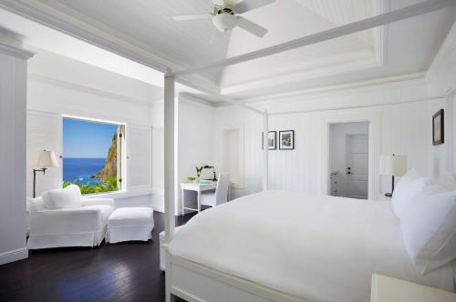 a white bedroom with a bed and a view of the ocean at Sugar Beach, A Viceroy Resort in Soufrière