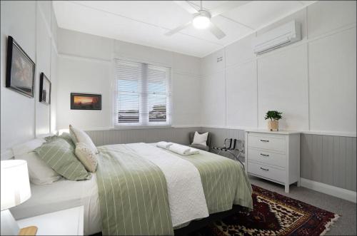 a white bedroom with a bed and a dresser at Lil's Cottage in Cessnock