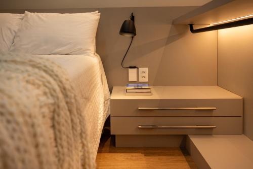 1 dormitorio con 1 cama y mesita de noche con lámpara en Studio Cosmopolita - Novo - possui automação, en Nova Santa Medianeira