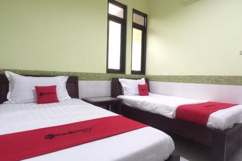 two beds with red and white sheets in a room at RedDoorz Syariah near Bypass Krian in Gabung