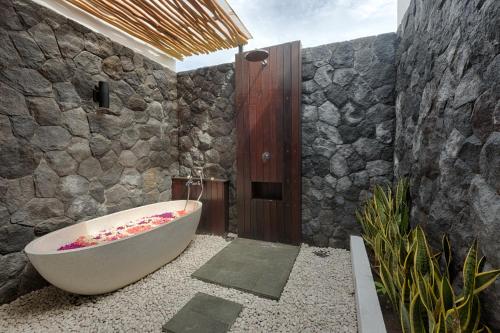 a bathroom with a bath tub and a stone wall at Lodji Ubud in Ubud