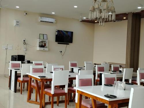 une salle à manger avec des tables et des chaises blanches et une télévision dans l'établissement Hotel Raipur Pride, à Raipur