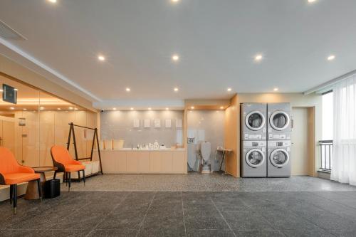 a laundry room with two washing machines and orange chairs at Atour X Hotel Chengdu Longquan Automobile City in Chengdu