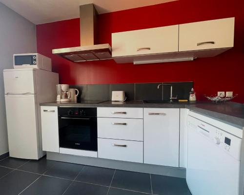 une cuisine avec des placards blancs et un mur rouge dans l'établissement L'instant Moderne Centre-ville Parking Gratuit, à Béziers