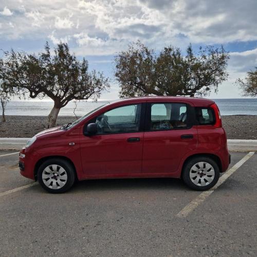a red car parked in a parking lot near the beach at Edelweiss Rent Rooms-Rent a Car in Tsoútsouros
