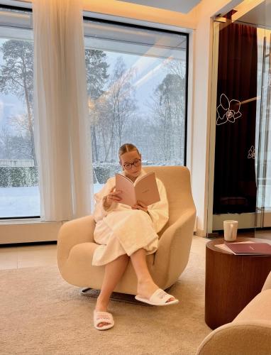 a woman sitting in a chair reading a book at Hotel Dolce La Hulpe Brussels in La Hulpe