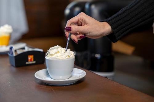 a woman stirring a cup of whipped cream with a spoon at Hotel Derby in Folgarida