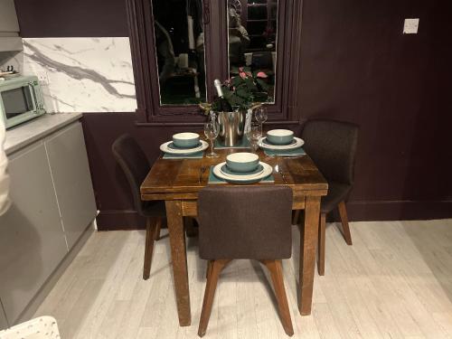 a wooden table with chairs and bowls and plates on it at Park View is a beautiful whole entire house close to town centre, sleeps 8 in 4 rooms, 2 doubles and 4 single beds with 2 shower rooms, available for holidays, insurance stays, trades people, contractors, pets welcome in Wisbech