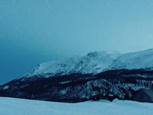 a mountain covered in snow with a house in the foreground at Sjarmerende tømmerhytte på gårdstun in Baukål