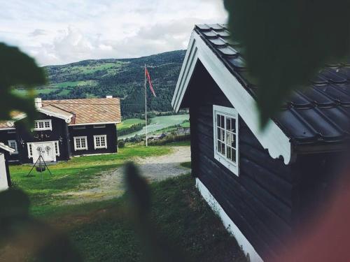 a black building with a white window and a house at Sjarmerende tømmerhytte på gårdstun in Baukål