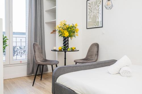 a bedroom with a bed and two chairs and a table with flowers at The Premium Stay - Duke Housing in Vitry-sur-Seine