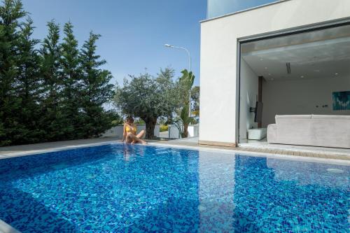 a woman sitting on the edge of a blue swimming pool at Seaview Luxury Villa Jacuzzi & Pool! 2 Min Beach in Protaras