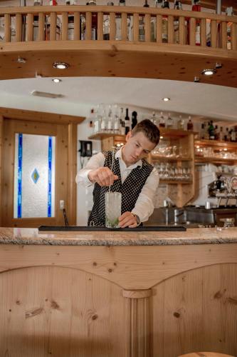 a man in a kitchen making a drink at Dolomites Nature Hotel Vigilerhof in Siusi