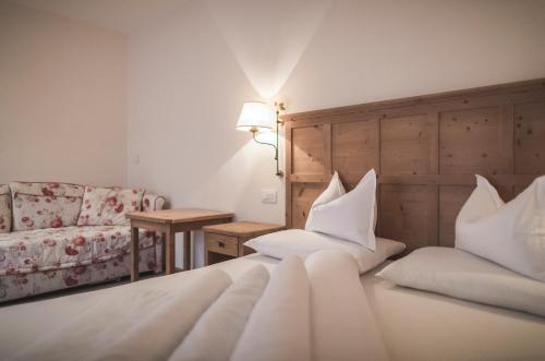 a bedroom with a bed with white sheets and a couch at Hotel Alpenhof in Rasùn di Sotto