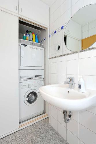a white bathroom with a sink and a washing machine at Ferienhaeuser Deichkrone in Bensersiel