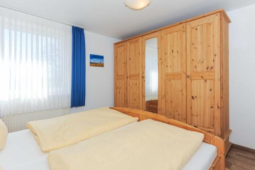 a bedroom with two beds and a wooden cabinet at Ferienhaeuser Deichkrone in Bensersiel