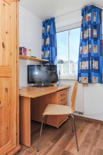 a desk with a television and a chair in a room at Ferienhaeuser Deichkrone in Bensersiel