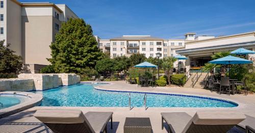 einen Pool mit Stühlen und Sonnenschirmen in einem Hotel in der Unterkunft Hilton San Antonio Hill Country in San Antonio