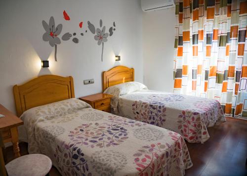 Habitación de hotel con 2 camas y flores en la pared en HOSTAL CACHE en Baza