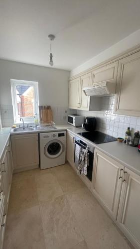 La cuisine est équipée de placards blancs et d'un lave-vaisselle. dans l'établissement Best Spot near Stratford, à Londres