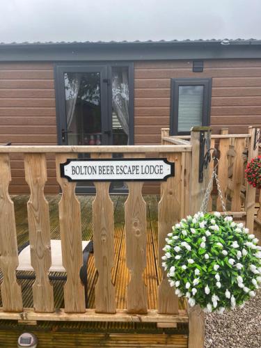 Bolton Beer Escape Lodge في Warton: سور خشبي مع وضع علامة على المنزل