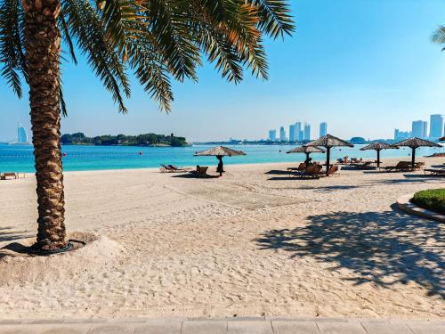 a beach with umbrellas and people sitting on the sand at Seaside Serenity Residence Elegant 1BR Escape in Palm Jumeirah by La Buena vida holiday homes in Dubai