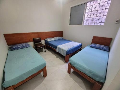 a room with two beds and a chair and a window at Guarujá Praia Hotel Econômico in Guarujá