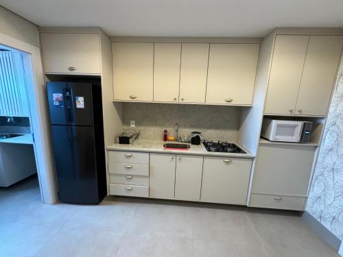 a kitchen with white cabinets and a black refrigerator at Flat próximo ao Shopping Campo Grande in Campo Grande