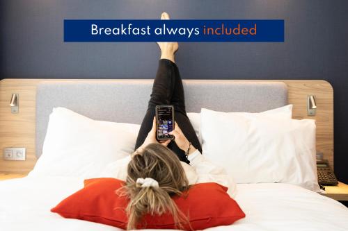 a woman laying on a bed holding a cell phone at Holiday Inn Express Antwerp - City Centre, an IHG Hotel in Antwerp