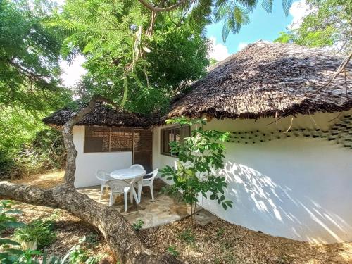 a cottage with a thatched roof and a table and chairs at Watamu Beach Cottages in Watamu