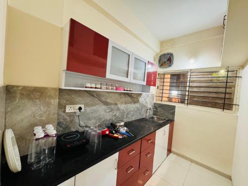a kitchen with red cabinets and a black counter top at Home Escape 1BHK Apartment Near Bombay Hospital in Indore