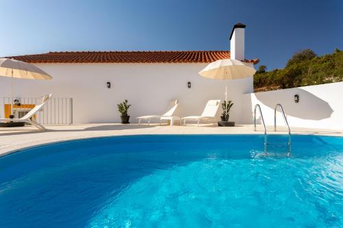 a pool with chairs and umbrellas next to a house at Casa da Azenha - Quinta do Boição - Private pool in Bucelas