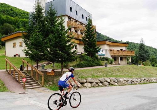 un hombre montando una bicicleta delante de un edificio en Résidence Routes du Monde ATC Saint-François-Longchamp, en Saint-François-Longchamp