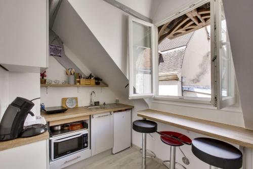 une cuisine avec des placards blancs, une fenêtre et des tabourets dans l'établissement L'Écrin de la Cathédrale, à Chartres